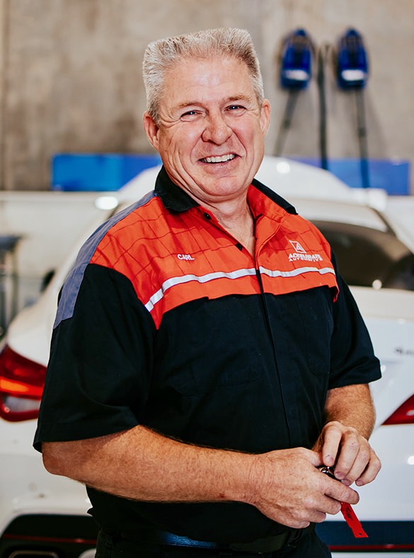 Carl Millward, a smiling man in a red and black uniform, stands proudly in front of a white car in the garage. Carl Millward, a smiling man in a red and black uniform, stands proudly in front of a white car in the garage.
