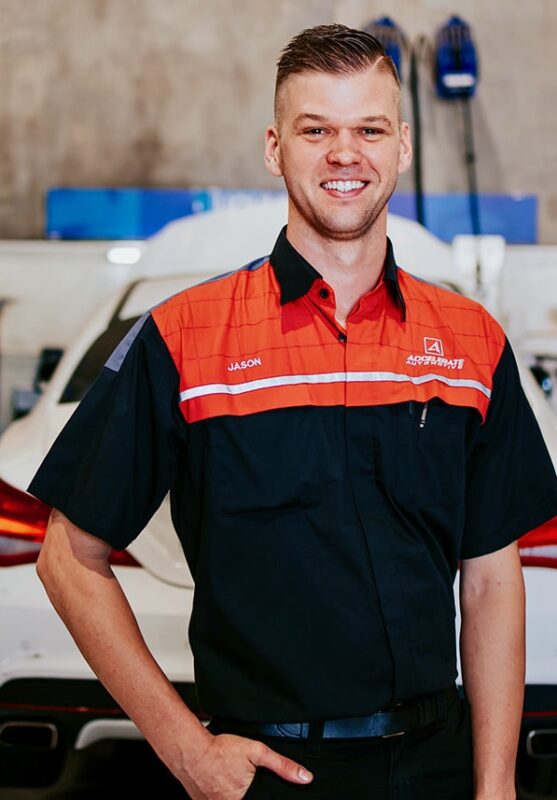 A person wearing a black and red work shirt with the name “Carl Millward” embroidered on it, standing in front of a white car in a garage setting. A person wearing a black and red work shirt with the name "Carl Millward" embroidered on it, standing in front of a white car in a garage setting.